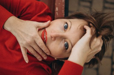 Parlak mavi gözleri ve parlak bir gülümsemesi olan neşeli bir kadın, canlı kırmızı bir kazak giymiş, açık havada poz veriyor. Pazarlama kampanyaları, web siteleri ve reklamlarda kullanım için harika. Özgünlük ve neşeli yaşam üzerine odaklı reklamlar..