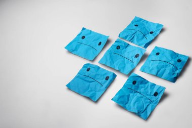 Beyaz arka planda hüzünlü, açık mavi kağıt yüzler. Mavi Pazartesi konsepti.