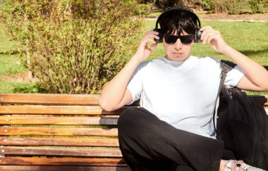 Park Bench 'te otururken kulaklık takan genç adam.