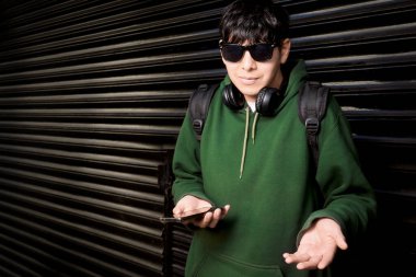 Yeşil kapüşonlu genç adam telefonu tutarken şaşkınlıkla hareket ediyor.