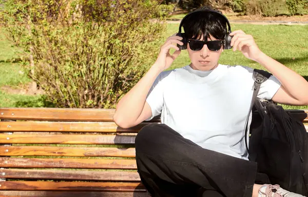 Park Bench 'te otururken kulaklık takan genç adam.