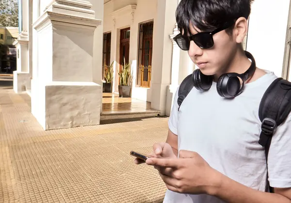 Boynunda kulaklıkla akıllı telefon kullanan genç adam.