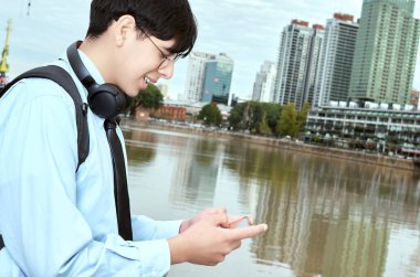 Gülümseyen Şehir Öğrencisi Arka planda Gökdelenlerle Nehir kenarında Mesaj Yazıyor