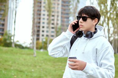 Urban Park 'ta elinde kahve tutarken telefonla konuşan genç adam.