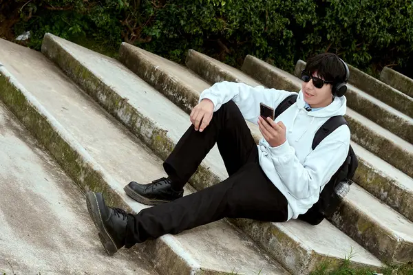 Genç adam kulaklıkları ve akıllı telefonuyla Apartman Basamaklarında Rahatlıyor