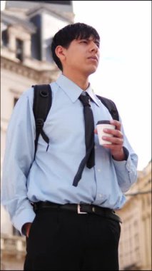  Resmi kıyafetli genç adam sokakta kahve içiyor.