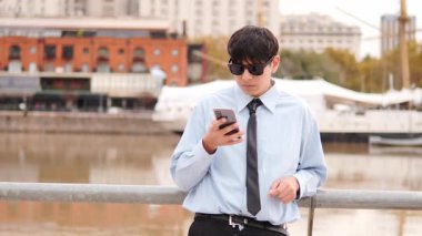  Riverside gezinti güvertesinde akıllı telefon kullanan genç adam.