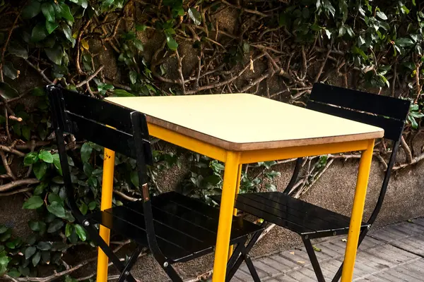 Sarı Masa ve Siyah Sandalyeler Kaldırımlar Bahçesinde Yapraklı Arka plan
