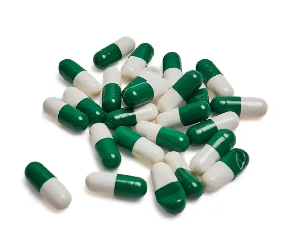 Beyaz arka planda izole edilmiş yeşil ve beyaz kapsül yığınları yüzeye saçıldı. Reçeteli terapi, tıbbi tedavi dozaj arzı ve uyuşturucu güvenliği bilincini gösteren ilaç konsepti.
