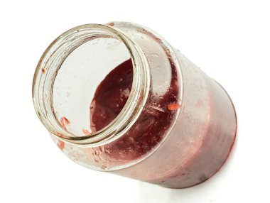 Kullanılmış çilek reçeli kavanozu, beyaz arka planda izole edilmiş meyve artıklarıyla eğilmiş.