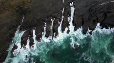 Drone View The Beauty of Waves Rocky Cliffs 'e çarpıyor. Bu drone görüntüsü kayalıklara çarpan dalgaların çarpıcı görüntüsünü yakalıyor. Beyaz dalgalarıyla berrak deniz suyu, karanlık kayalara karşı güzel bir kontrastlık yaratır..