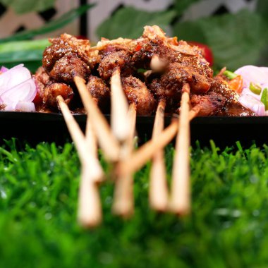 Fıstık soslu lezzetli tavuk satay, kızarmış arpacık soğanıyla süslenmiş, taze domates, arpacık soğanı, acı biber ve limon dilimleri ile servis edilmiş siyah bir tabakta muz yaprağı üzerinde..