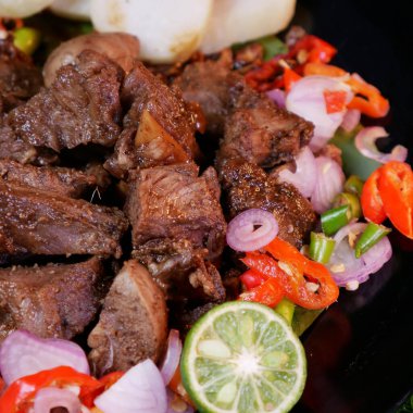 Kızarmış arpacık soğanı ve kırmızı soğan serpilmiş mükemmel baharatlı keçi, yanında pirinç kekleri, limon dilimleri ve muz yaprağında taze domatesler..