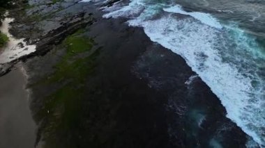 Sert dalgaların sert siyah kayalara çarptığı kayalık bir sahilde insansız hava aracı hareketi güzel görünüyor ama çok tehlikeli. Banten, Endonezya Sawarna plajı..