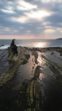 Gün batımına doğru havadan görüntü hareketi. Tanjung Layar Sawarna Sahili, Banten, Endonezya 'da ikonik bir turizm merkezi. Tekne yelkeni şeklinde metamorfik çökeltilerden oluşan kayalar..