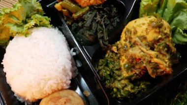 Nasi Padang 'ı siyah kutuda kapamak Padang' ın geleneksel yiyeceğidir. Endonezya 'da. Ahşap bir kasede pişirme baharatları, kırmızı çiçekler ve sentetik otlarla süslenmiş..