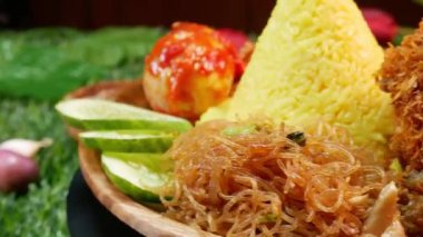 Yakın koni şeklinde sarı pirinç, kızarmış tavuk, kırmızı sambal, sambal yumurtası, kızarmış vermicelli, taze salatalık dilimleri, kırmızı soğan, sarımsak ve küçük kaselerde biber ile servis edilir..