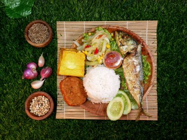 Top view, complete Mixed Rice or Nasi Campur served with white rice, fried fish, tempeh, tofu, fresh vegetables, sambal, and spices on a bamboo mat. clipart