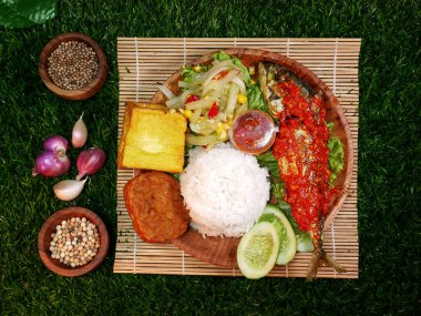 Top view, complete Mixed Rice served with white rice, fried fish in spicy red sambal, tempeh, tofu, fresh vegetables, sambal, and spices on a bamboo mat. clipart