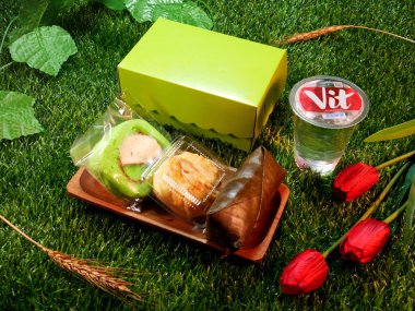 Jakarta, Indonesia. December 24, 2024. Snack box package traditional Indonesian cakes, cream puffs, roll cakes, and lemper delicious and a glass of mineral water, with a natural decorative touch clipart