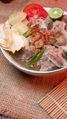 Closeup oxtail soup or sop buntut with potatoes, tomatoes, lime slices, and fried shallots. Served on a bowl white with Bamboo mat and burlap. Space for text available clipart