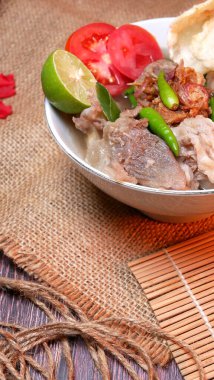 Close up beef rib soup or Iga soup with clear broth with beef, potato, fresh tomato, lime, green chilies, fried onions, and crackers. Served in a white bowl with unique decoration. Space for text available