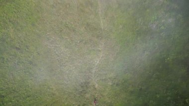 Havada yüzen ince bir sis ile tropik bir dağın ortasında yürüyen kırmızı sırt çantalı bir yürüyüşçünün hava görüntüsü huzurlu ve sakin bir atmosfer yaratıyor..