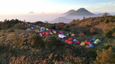Drone renkli dağcı çadırlarıyla Prau Dağı çayırlarında uçuyor. Sindoro Dağı, Sumbing Dağı ve diğer dağların güzel manzarası nedeniyle burası kamp için gözde bir yerdir..
