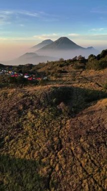 Şafak vakti Prau Dağı 'nın güzelliği. Tırmanışçıların kamp yaptığı çayırın üzerinde uçan insansız hava aracı. Sindoro Dağı ve Sumbing Dağı görülebilir yüksekliktedir. Sabahları ince bir sis tabakasıyla kaplıdır..