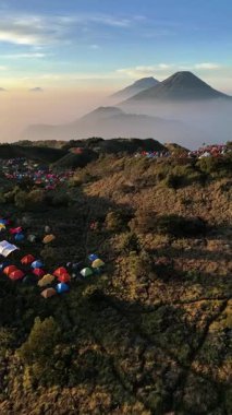 Prau Dağı 'nda şafak vakti güzel ve çarpıcı doğal manzara. Dağcıların renkli çadırları ayakta duruyor. Sindoro Dağı, Sumbing ve diğer dağlar ince bir sis bulutuyla örtülmüş olarak görülür..