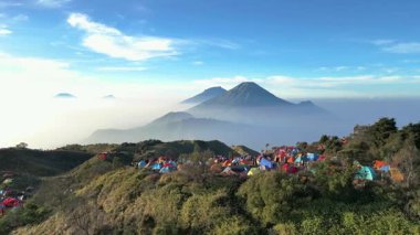 Drone 'dan hava görüntüsü, Mount Sindoro' nun güzel ve çarpıcı manzarası ve şafak vakti Prau Dağı 'ndaki kamp alanından Sumbing. Renkli dağcı çadırları soğuk bir sabahta ilginç bir kontrastlık yaratır..