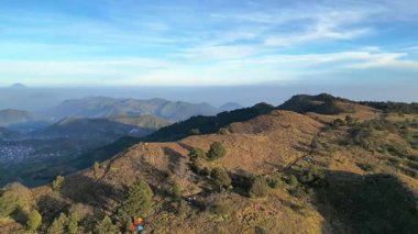 Hava manzarası, şafak vakti Prau Dağı 'nın doğal manzarası mavi bulutlu bir gökyüzü, renkli çadırlar, romantik ince sis, ağaçlar ve yeşil çayırlar. Ünlü Dieng Platosu uzaklardan görülebiliyor..