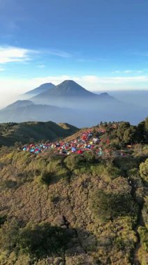 Drone 'dan hava görüntüsü, Mount Sindoro' nun güzel ve çarpıcı manzarası ve şafak vakti Prau Dağı 'ndaki kamp alanından Sumbing. Renkli dağcı çadırları soğuk bir sabahta ilginç bir kontrastlık yaratır..