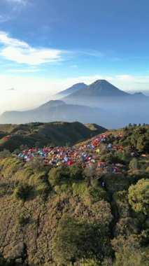 Drone 'dan hava görüntüsü, Mount Sindoro' nun güzel ve çarpıcı manzarası ve şafak vakti Prau Dağı 'ndaki kamp alanından Sumbing. Renkli dağcı çadırları soğuk bir sabahta ilginç bir kontrastlık yaratır..