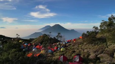 Drone 'dan hava görüntüsü, Mount Sindoro' nun güzel ve çarpıcı manzarası ve şafak vakti Prau Dağı 'ndaki kamp alanından Sumbing. Renkli dağcı çadırları soğuk bir sabahta ilginç bir kontrastlık yaratır..