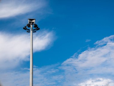 Metal direğin üzerindeki modern sokak lambaları bulutlu mavi gökyüzü arkaplanıyla otoyolu aydınlatmak için. Aydınlatmanın yanı sıra sokak lambaları kamu güvenliği olarak çok işlevseldir..