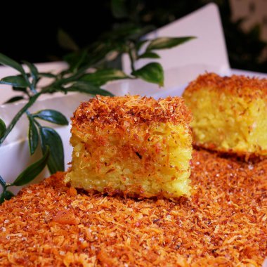 Yakın plan Ketan Kuning (Sarı Yapışkan Pirinç), genellikle Serundeng olarak bilinen tatlı ve tuzlu bir tadı olan rendelenmiş hindistan cevizi serpiştirilmiş geleneksel Endonezya yemeği. Beyaz bir karton kutuda servis edilmiş..