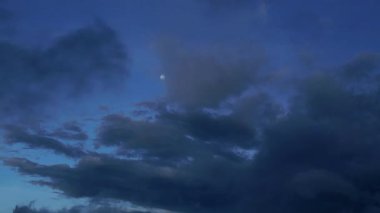 Fırtınadan önce gökyüzünün bir panoraması. Dolunay, kalın bulutlar arasında parıldıyor. Rüzgarda hafifçe hareket ediyor. Koyu mavi ve gri bulutlar dramatik ve gizemli bir atmosfer yaratır..