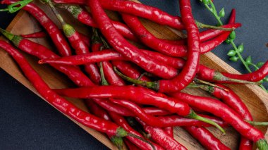 Siyah arka planlı ahşap tepside taze yeşil saplı uzun kıvırcık kırmızı biber manzarası. Yemek pişirmeye ya da yemek pişirmeye uygun.
