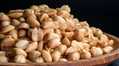 Ahşap bir tabakta, çıtır çıtır ve tuzlu kabuklu fıstıkların ayrıntıları siyah arka planda, atıştırmalıklar için uygun, Kurban Bayramı teması, ya da aşçılık teması.