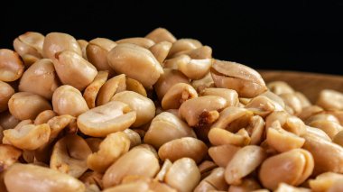 Koyu bir zemin üzerinde ahşap bir tabakta kavrulmuş fıstık yığınına yakın plan. Atıştırmalık, sağlıklı yemek veya aşçılık kavramları için uygun..