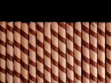 Koyu arkaplanda çizgili spiral desenli, düzgün düzenlenmiş çikolatalı gofret rulolarının üst görüntüsü. Reklam ve tanıtım için uygun..