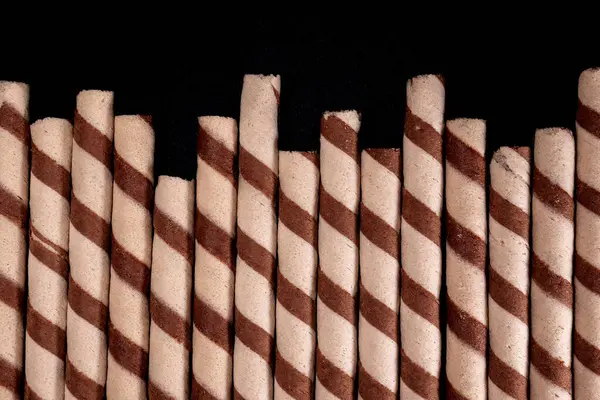 Koyu arkaplanda çizgili spiral desenli, düzgün düzenlenmiş çikolatalı gofret rulolarının üst görüntüsü. Reklam ve tanıtım için uygun..