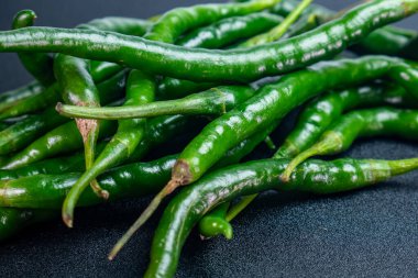 Koyu bir yüzeyde uzun, çiğ yeşil biber yığını, cildin doğal tazeliğini ve parlak dokusunu vurguluyor..