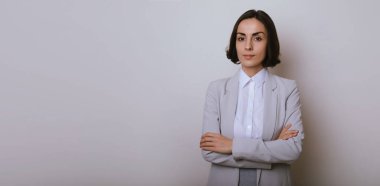 Stüdyo, gri arka planda kollarını kavuşturmuş güzel bir iş kadınının portresi.