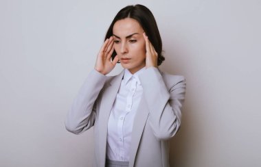 Gri arka plan üzerinden izole edilmiş genç iş kadını şiddetli baş ağrısı, çaresiz ve stresli çünkü iş yerindeki sorunlar sonrasında ağrı ve migren.