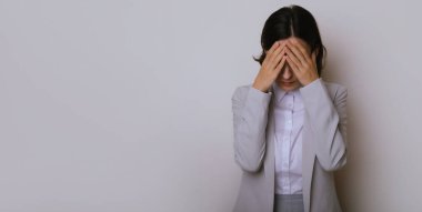 Gri arka plan üzerinden izole edilmiş genç iş kadını şiddetli baş ağrısı, çaresiz ve stresli çünkü iş yerindeki sorunlar sonrasında ağrı ve migren.