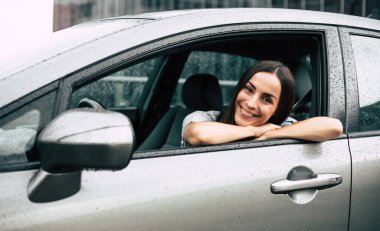 Satıcıdan yeni bir araba alan genç ve mutlu bir kadın. Heyecanlı otomobilin sahibi. Gülümseyen kadın aracını kullanıyor.