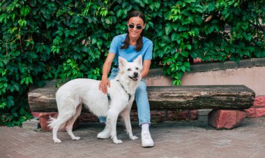 Gözlüklü mutlu genç bayan dışarıda sevimli beyaz tüylü köpeğiyle oynuyor. Evlat edinme, kurtarılma, barınma, yoldaş, evcil hayvan.