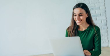 Gündelik giysiler içinde genç, kendine güvenen bir bayan bir dizüstü bilgisayar kullanıyor ve gri arka planda yerde otururken gülümsüyor. Eğitim, eğitim, üniversite, üniversite, mezuniyet konsepti